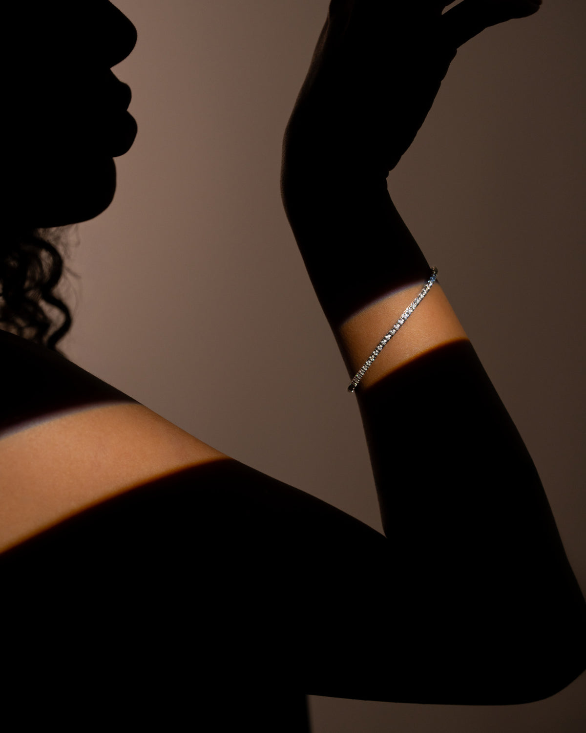 Bracciale tennis diamanti oro bianco 18 carati indossato al polso, braccio sollevato in controluce su fondo scuro