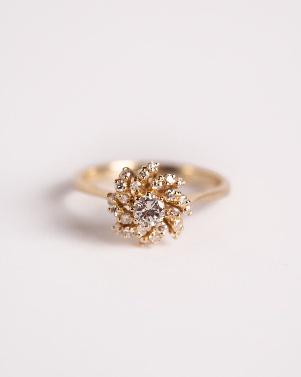 Anello solitario con diamante in oro giallo 18 carati e raggiera di diamanti, still life su fondo chiaro, Gioielleria La Rosa