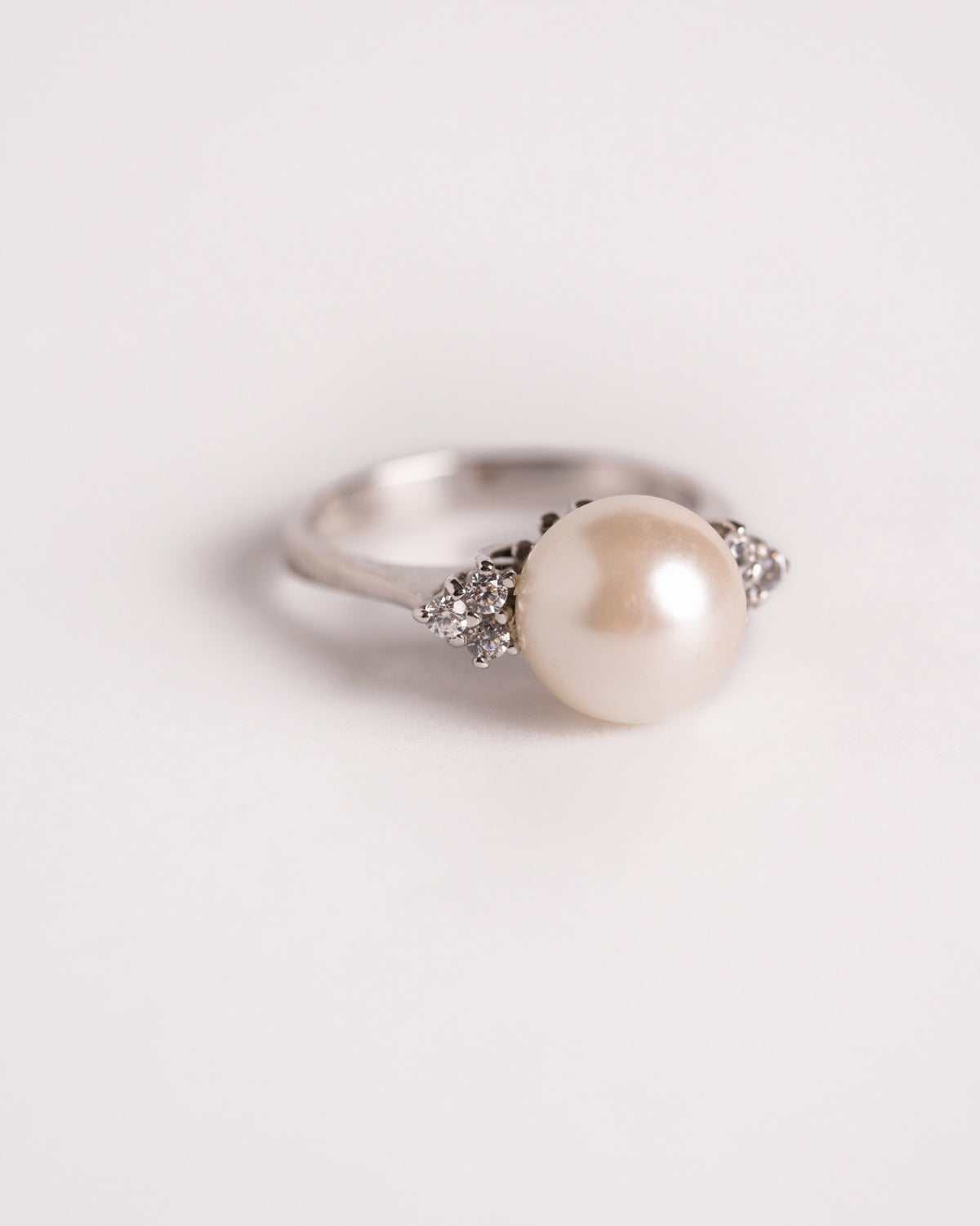 Anello con perla e diamanti in oro bianco visto di tre quarti, con i piccoli diamanti accanto alla perla, su fondo chiaro