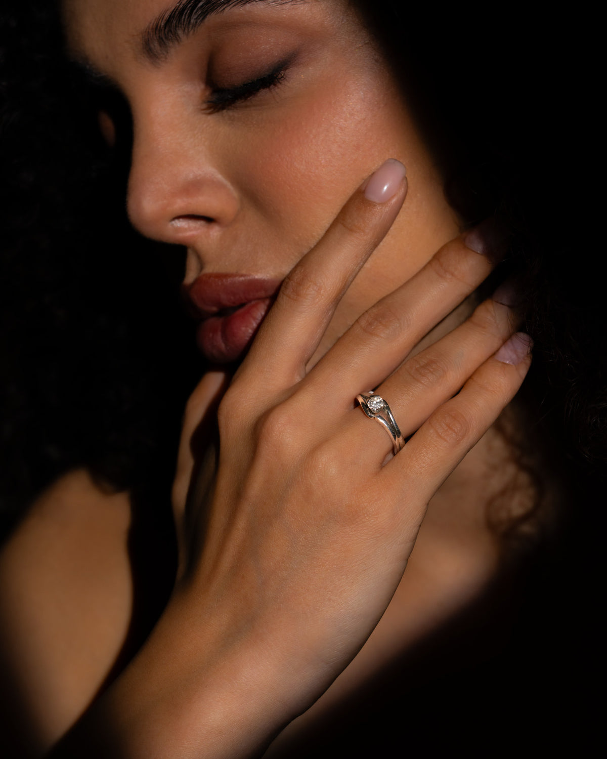 Anello solitario diamante oro bianco indossato al dito, mano appoggiata al viso su fondo scuro