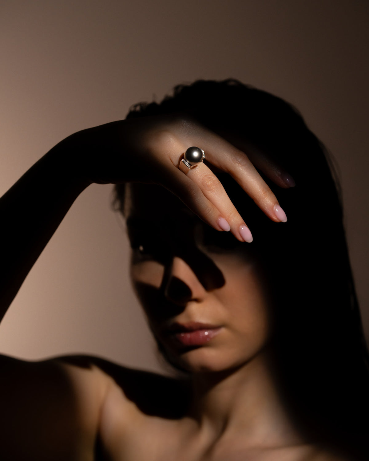 Anello Perla d'Ombra con perla di Tahiti al dito, mano sollevata davanti al viso tra luce e ombra, Gioielleria La Rosa