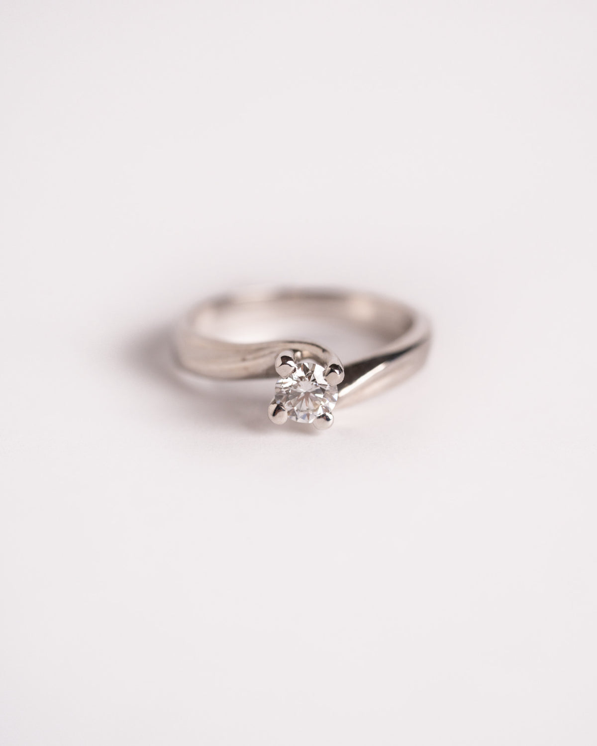 Anello solitario con diamante in oro bianco 18 carati Abbraccio di Luce, montatura avvolgente, still life su fondo chiaro