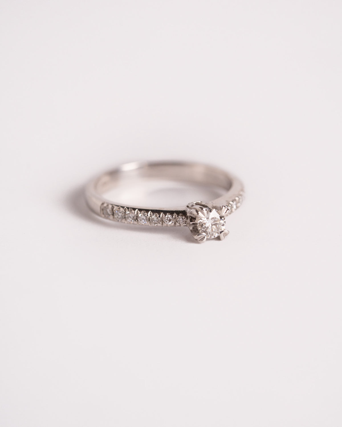 Anello solitario con brillanti nel gambo in oro bianco 18 carati, diamanti 0,23 ct totali, still life su fondo chiaro
