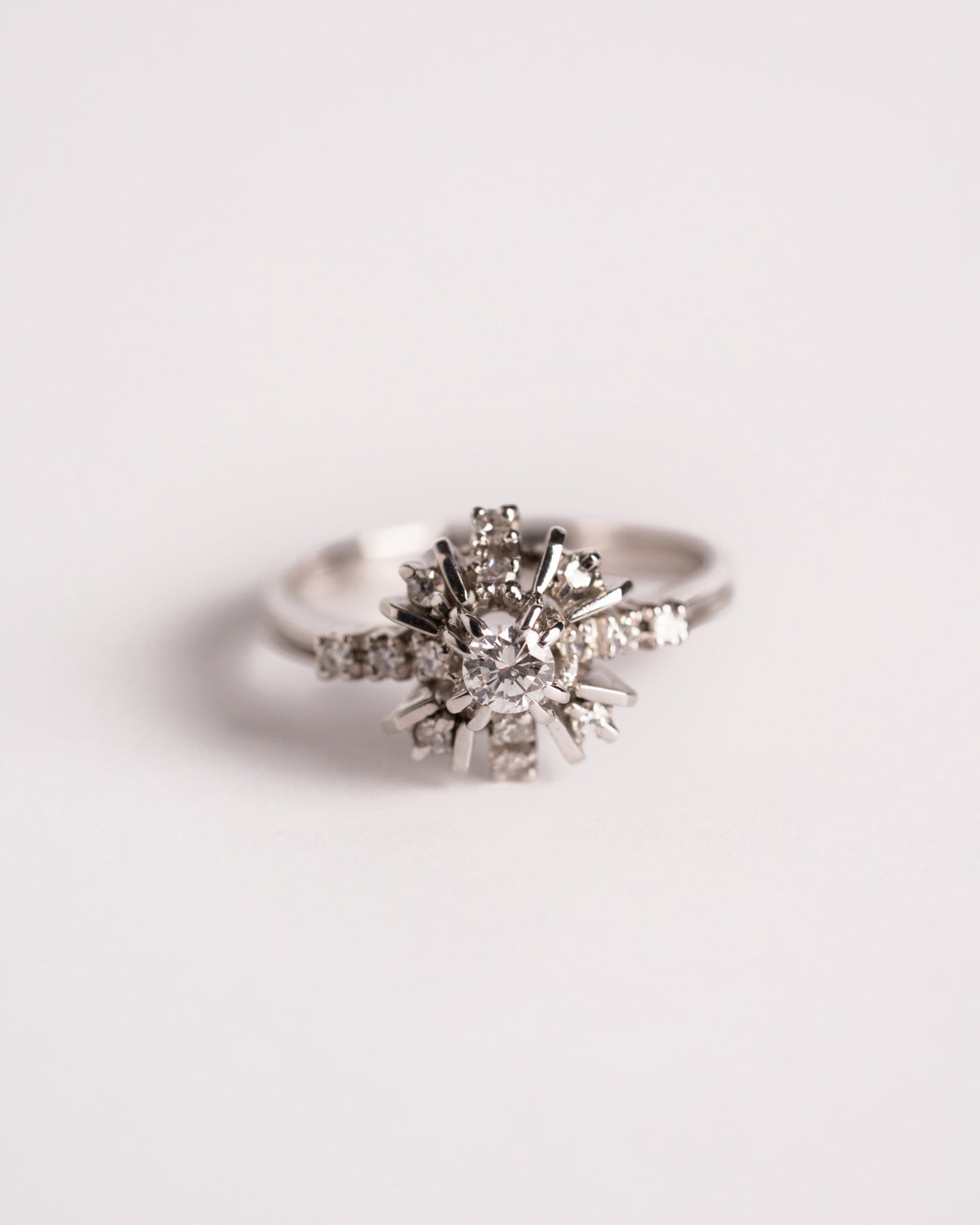 Anello a fiore con diamanti in oro bianco 18 carati, diamante centrale e montatura a raggi, still life su fondo chiaro