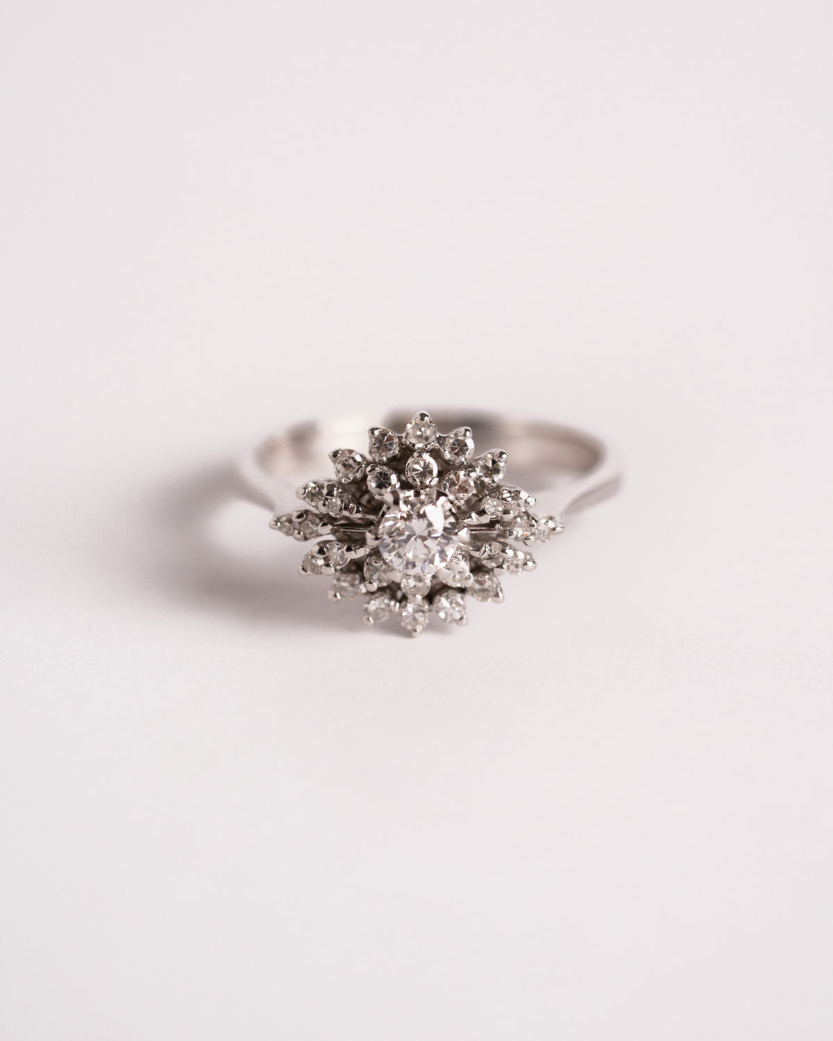 Anello a fiore con diamanti in oro bianco, diamante centrale e doppia corona di pietre, still life su fondo chiaro