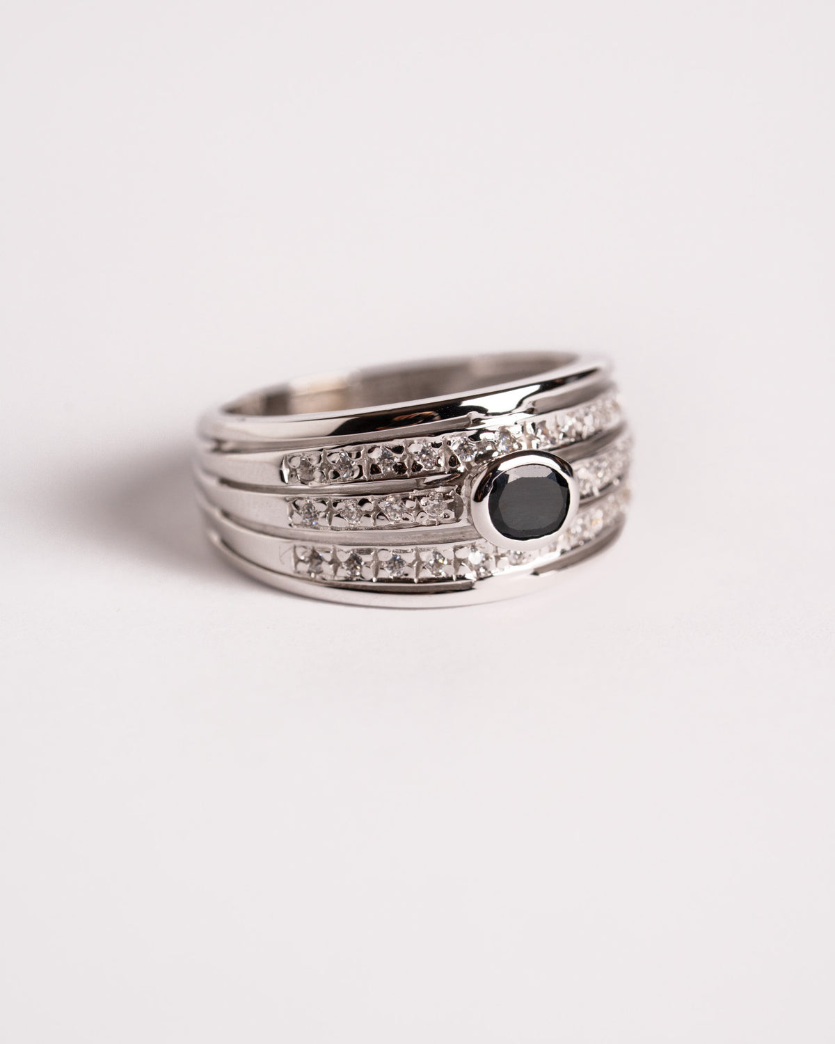 Anello fascione in oro bianco con tre file di diamanti e pietra nera, still life su fondo chiaro, Gioielleria La Rosa