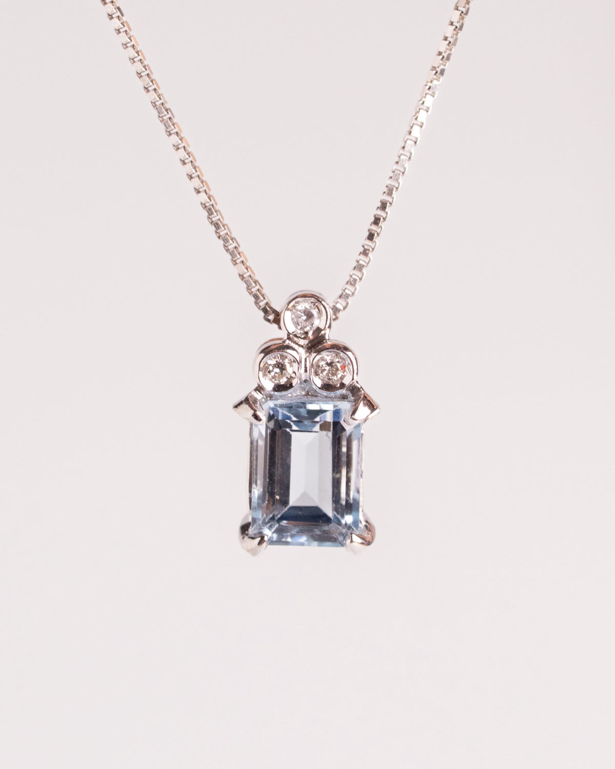 Collana con acquamarina e diamanti in oro bianco, ciondolo con pietra azzurra su catena sottile, still life su fondo chiaro