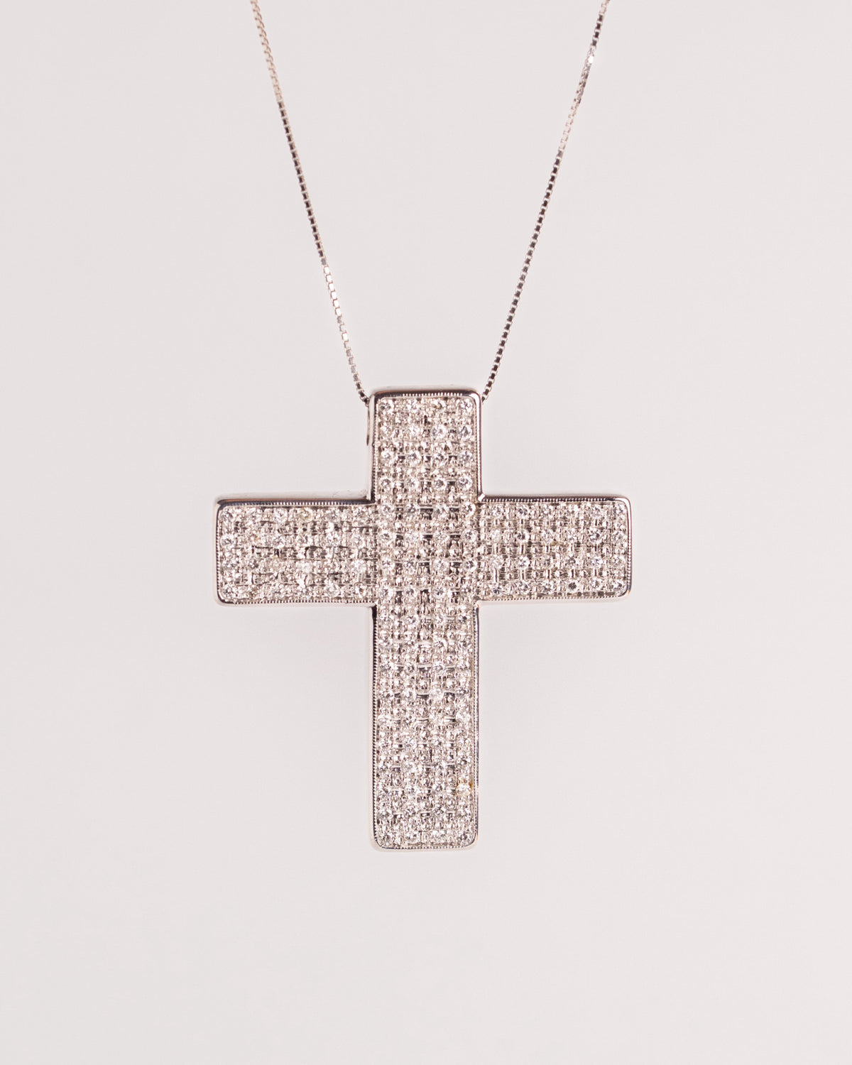 Ciondolo croce in oro bianco con pavé di diamanti e catena a maglia veneziana, still life su fondo chiaro